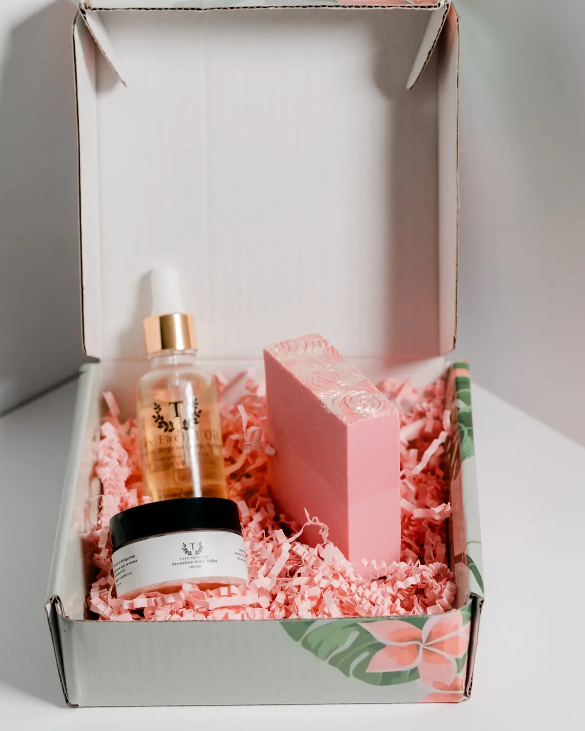 The Beauty Essentials Kit in its box: facial oil, a pink soap and a trial balm in pink paper